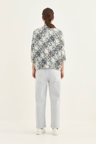 A model viewed from the back wearing a black and white abstract patterned button-up shirt, light gray trousers by Verge, and white sneakers, set against a plain white studio background.