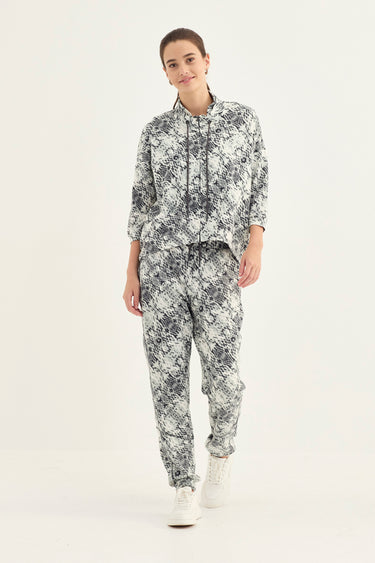A woman modeling a matching two-piece set with a snake print jacket pattern, featuring a long-sleeve top and pants by Verge, against a plain white studio background.