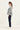 A woman in profile wearing a snake print jacket pattern long-sleeve top, dark navy jeans by Verge, and white sneakers, standing against a plain off-white studio background.