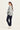 A woman is shown from a side-back angle wearing a snake print sweater and dark blue jeans by Verge, and white sneakers against a plain white studio background.
