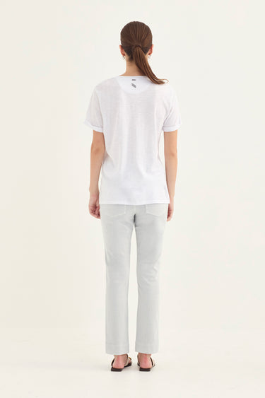 A woman viewed from behind wearing a white short-sleeve t-shirt and light gray straight-leg pants by Verge against a plain white studio background.