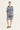 A woman modeling a short-sleeve button-front tunic dress by Verge with an abstract blue, white, and gray pattern, paired with black slide sandals, against a plain light background.
