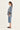A woman shown in profile wearing a blue and white patterned long-sleeve top, light blue cropped jeans by Verge, and black flat mules against a plain off-white studio background.
