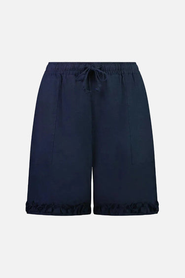 A model wearing a blue linen ruffle short by Verge with an elasticated waist and side pockets, paired with a solid color top and white sneakers.